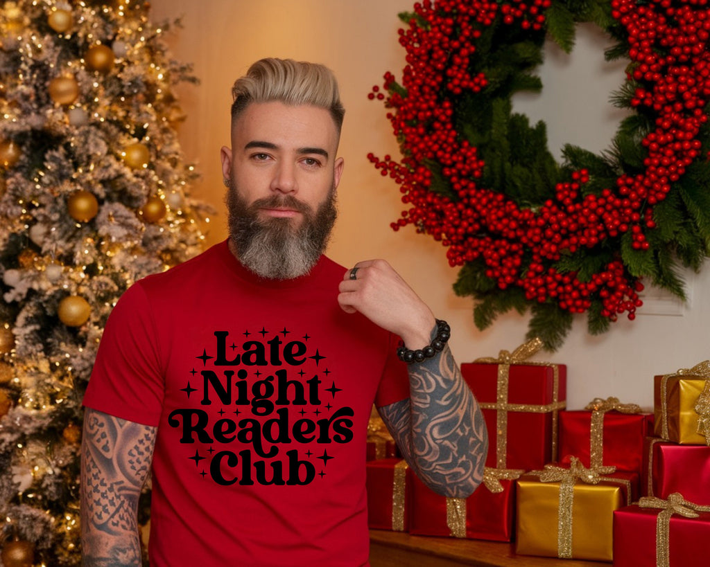 Man wearing a red 'Late Night Readers Club' t-shirt in front of Christmas decorations.