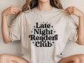 Person wearing a beige t-shirt with 'Late Night Readers Club' text.