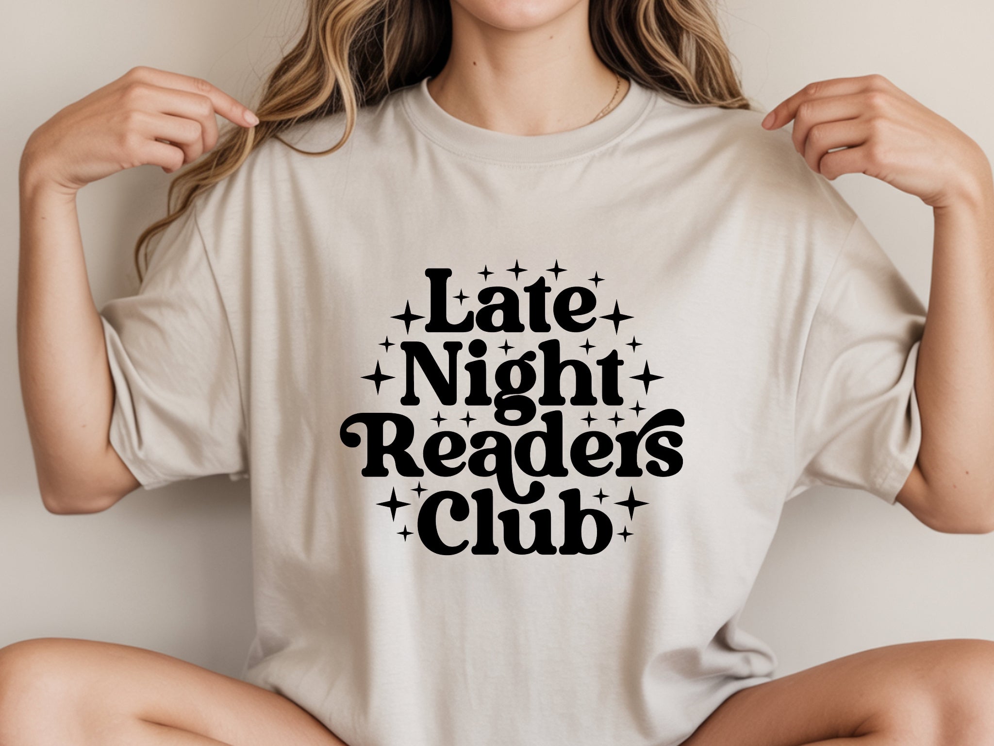 Person wearing a beige t-shirt with 'Late Night Readers Club' text.