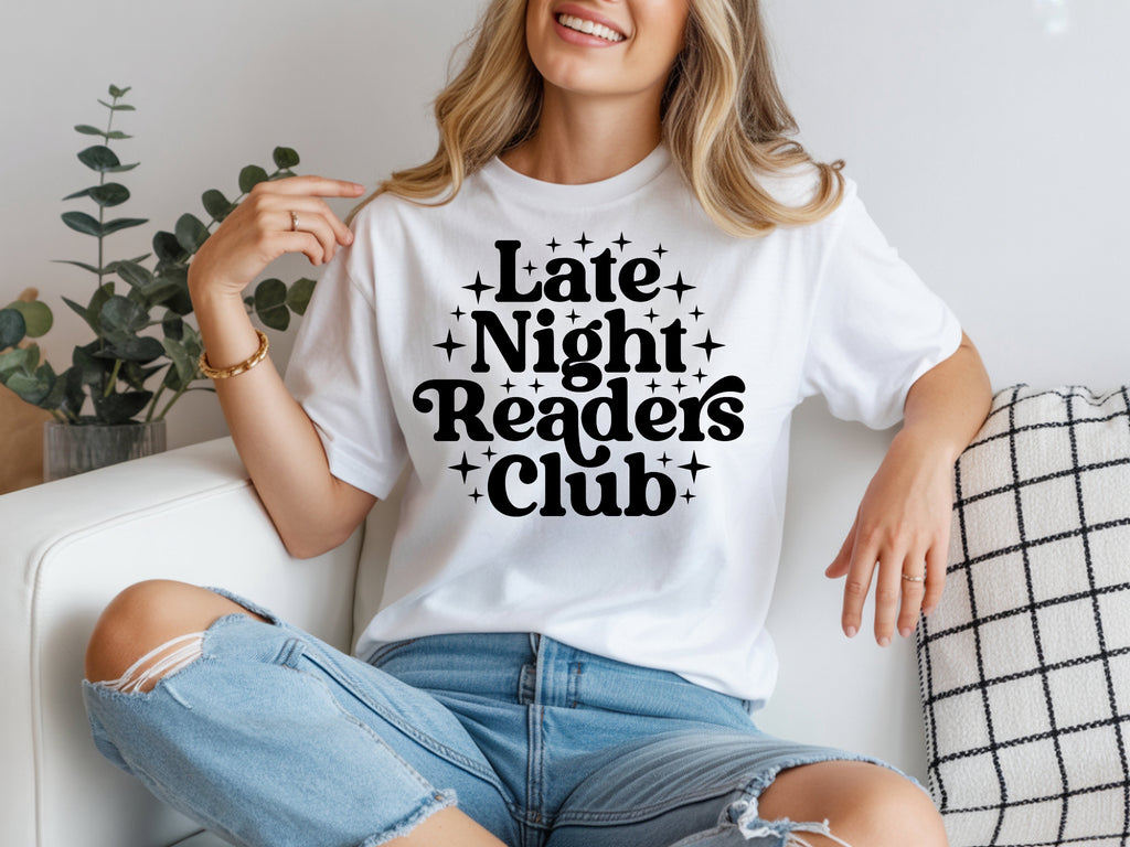 Person wearing a white t-shirt with 'Late Night Readers Club' text, sitting on a couch.