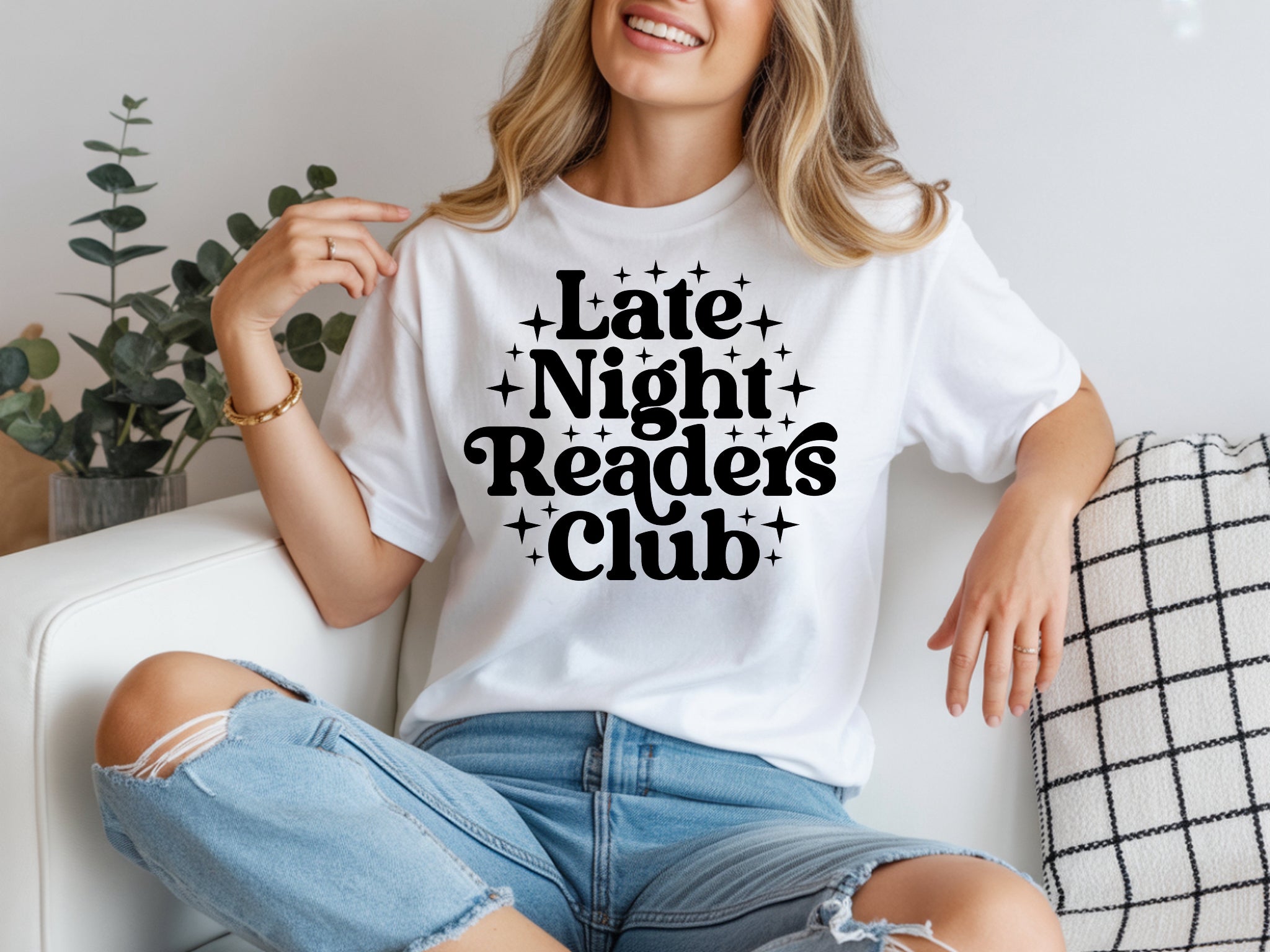 Person wearing a white t-shirt with 'Late Night Readers Club' text, sitting on a couch.